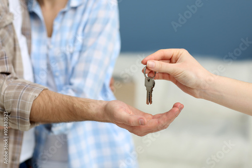 Female hand giving keys from new apartment to male hand on blurred background