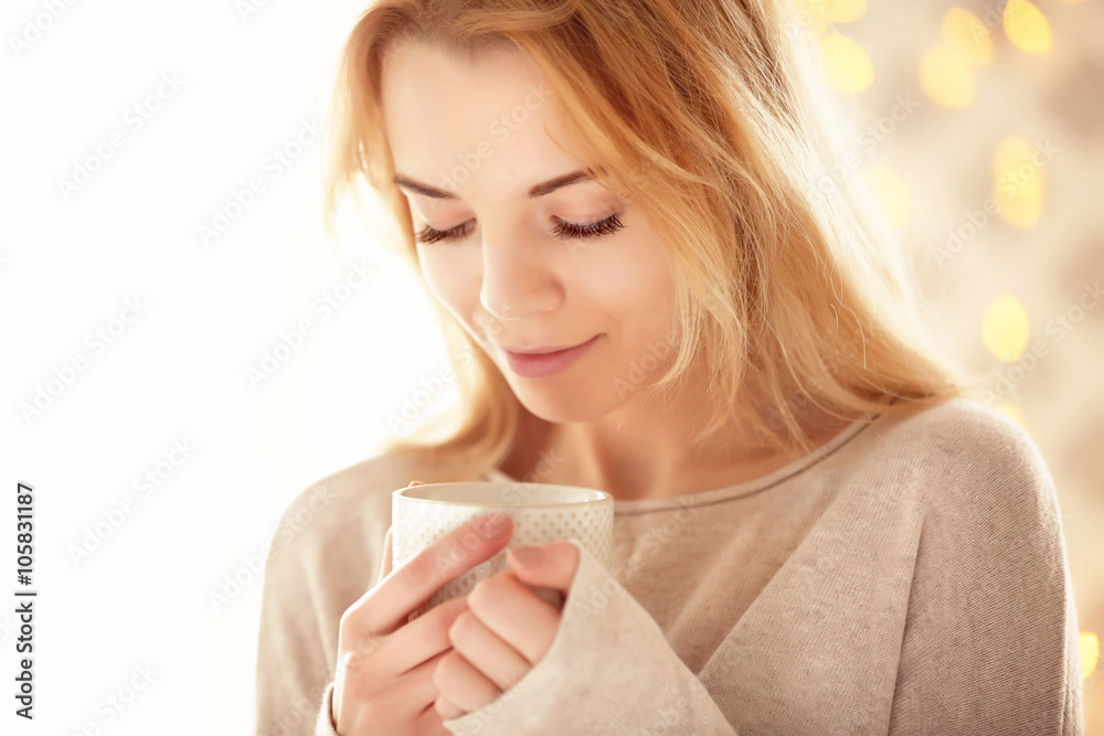 Blonde beautiful smiling girl enjoying her cup of hot delicious coffee or tea on the light background Blonde beautiful smiling girl enjoying her cup of hot delicious coffee or tea on the light background