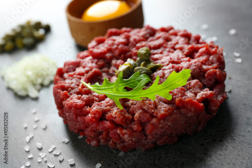 Beef tartare served with an egg yolk on a grey surface, close up photo
