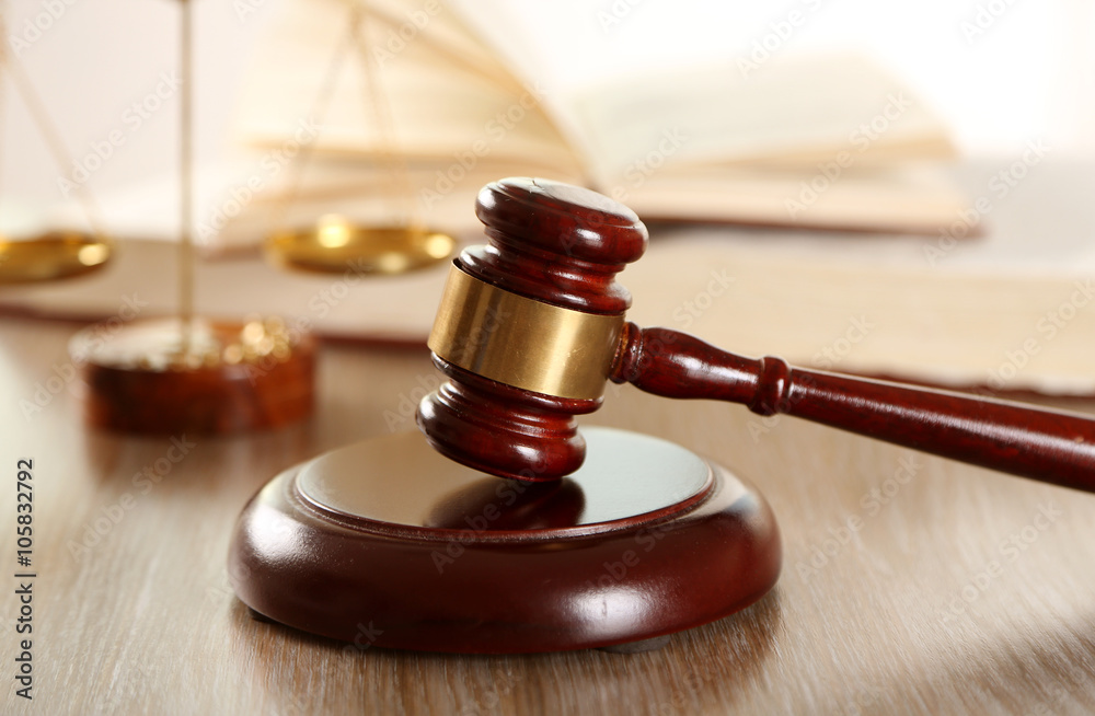 Gavel with books and scales of justice on wooden table closeup