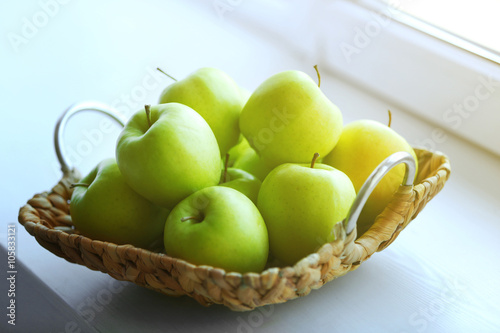 Ripe green apples in a wicker basket on windowsill