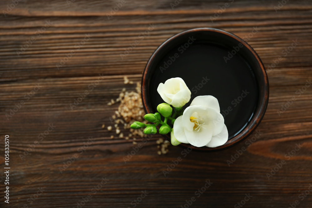 Beautiful flower in the bowl with water and sea salt on wooden background