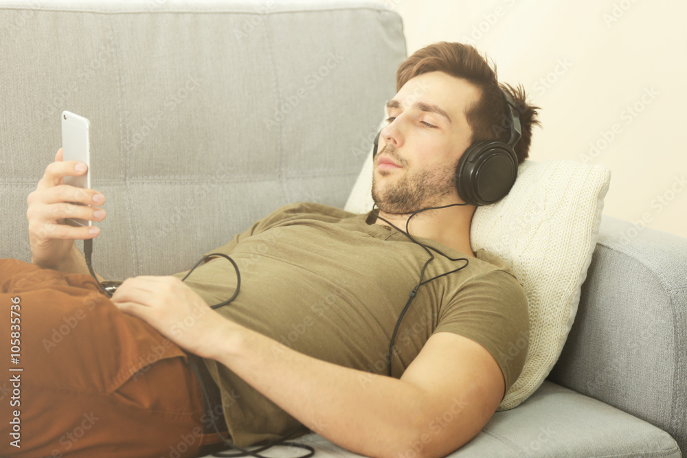 Obraz premium Young handsome boy listening music while lying on sofa