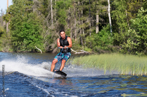 Fototapeta Naklejka Na Ścianę i Meble -  Young man riding wakeboard on a summer lake