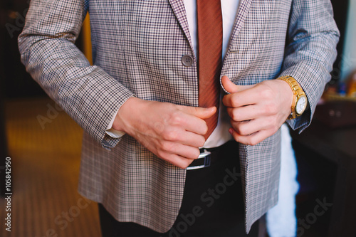 The man in the tie, straightens his plaid suit, close. Hands of the groom