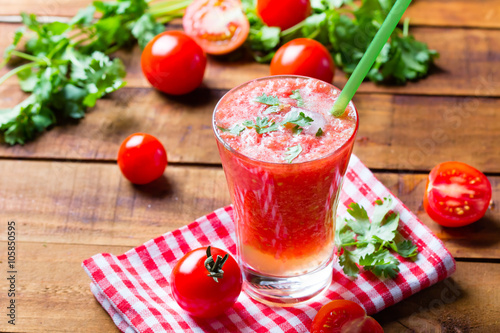 Gass of tomato smoothie, fresh tomatoes and cilantro on a dark wooden background . Vegetarian or healthy eating concept