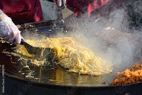 Man fries noodles on big frying pan, on street photo