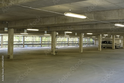Lit by the sickly glow of cheap fluorescent tubes, an underground parking garage stands almost empty , one car is left.