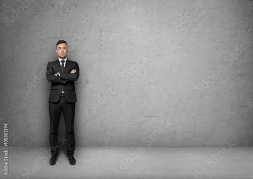 Young man in business suit, standing front of the concrete wall background. Business concept