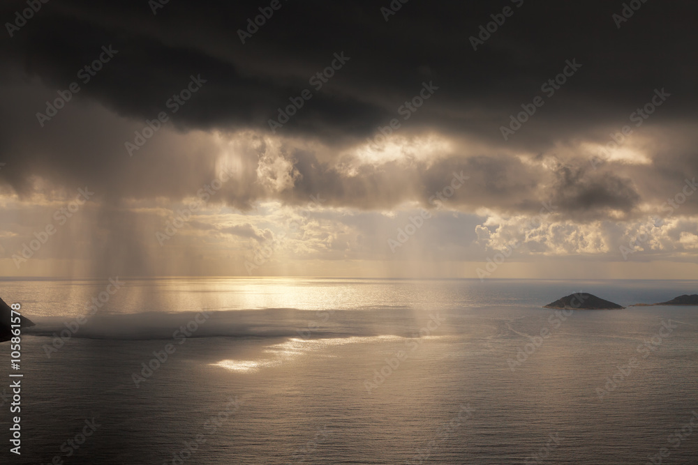 Rain shower and sun light beams through the dark clouds over the sea Rain shower and sun light beams through the dark clouds over the sea