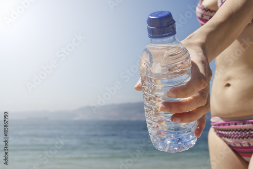 Woman's hand holding bottle of water under the sun