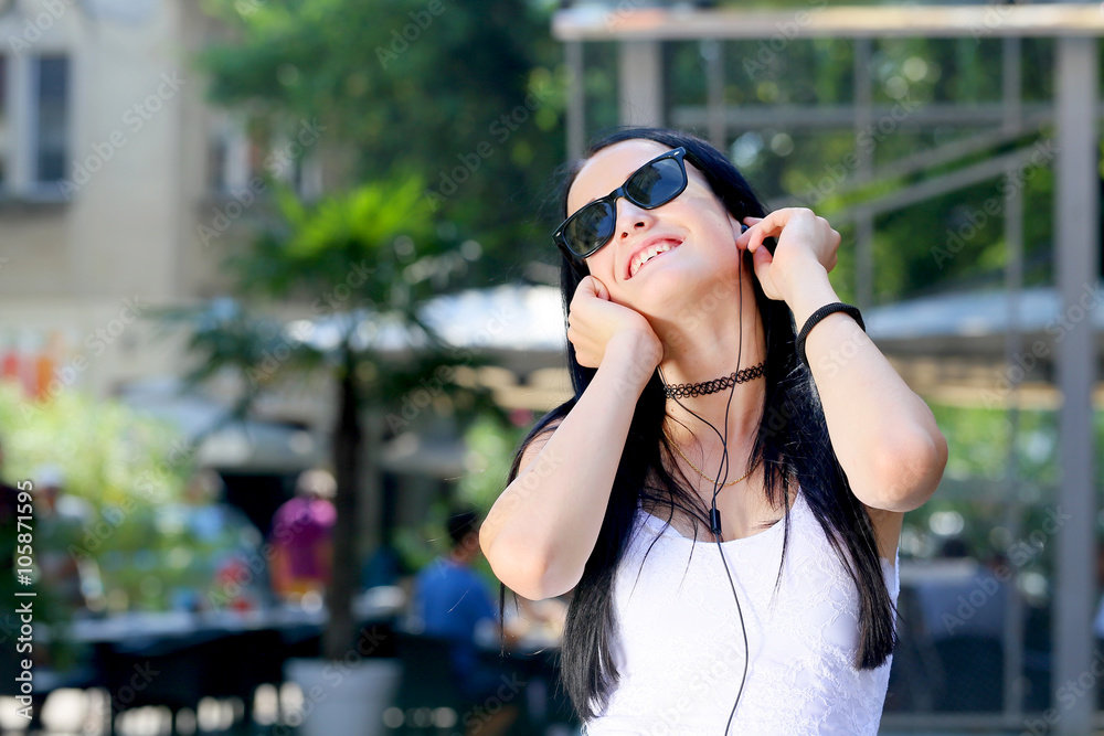 Fototapeta premium beautiful young black hair woman with sunglasses listening music with earphones in the city