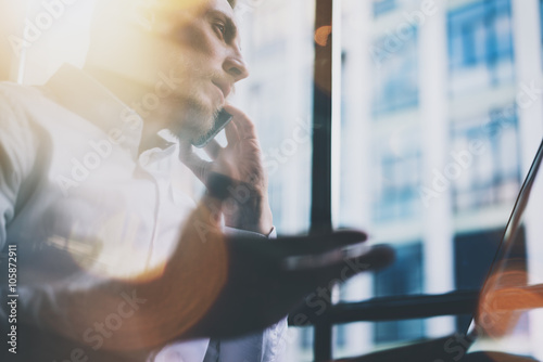 Closeup photo bearded adult businessman working on modern loft office. Man wearing white shirt and using contemporary smartphone. Panoramic windows background. Horizontal, film effect, bokeh