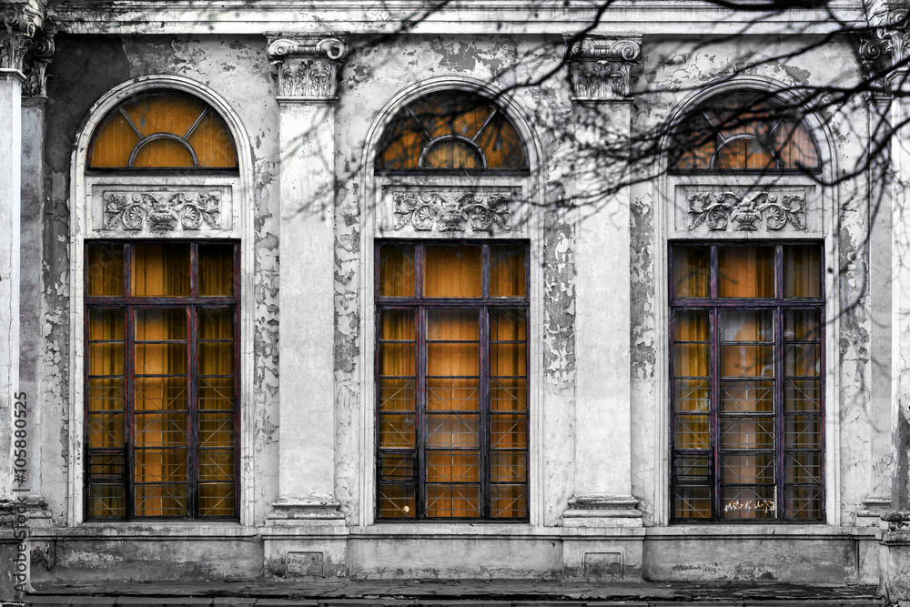 Facade of old abandoned building with three large arched windows of orange glass. Monochrome background