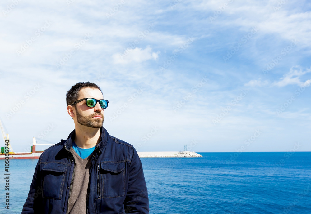 Portrait of man in spring clothes wearing sunglasses on sunny day by sea Portrait of man in spring clothes wearing sunglasses on sunny day by sea