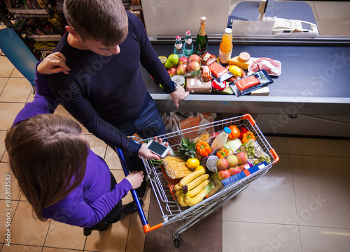 Obraz na plátně Young couple putting goods on counter in supermarket