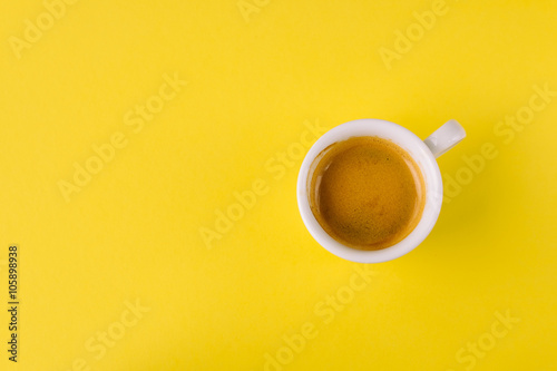 Small cup of coffee on bright yellow background, top view
