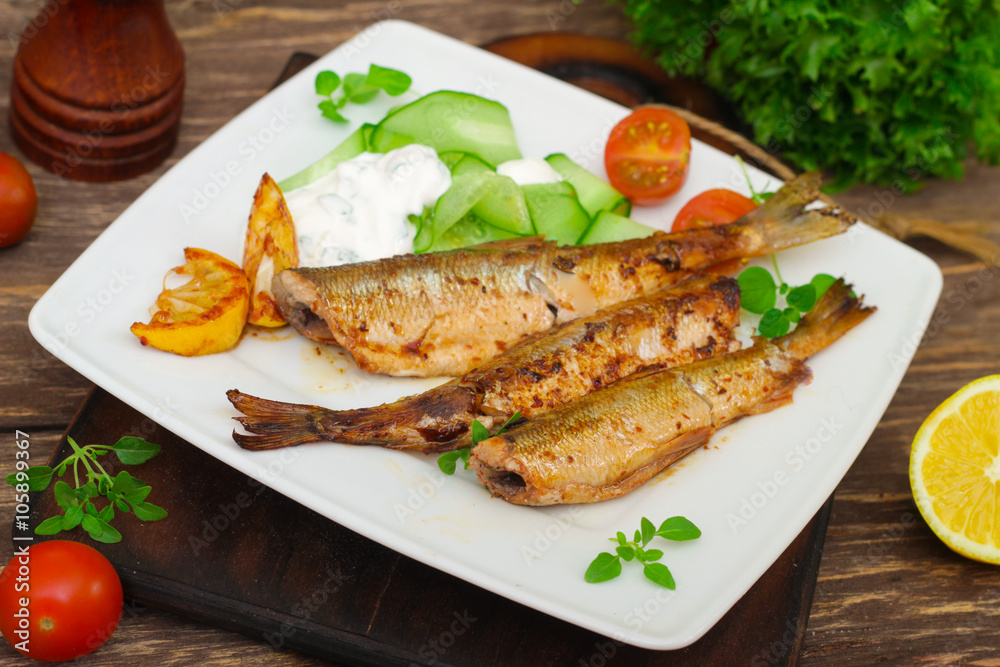 Roasted sardines with a salad of cucumber and yogurt on a wooden background. Mediterranean cuisine Roasted sardines with a salad of cucumber and yogurt on a wooden background. Mediterranean cuisine