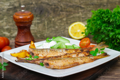 Roasted sardines with a salad of cucumber and yogurt on a wooden background.  Mediterranean cuisine