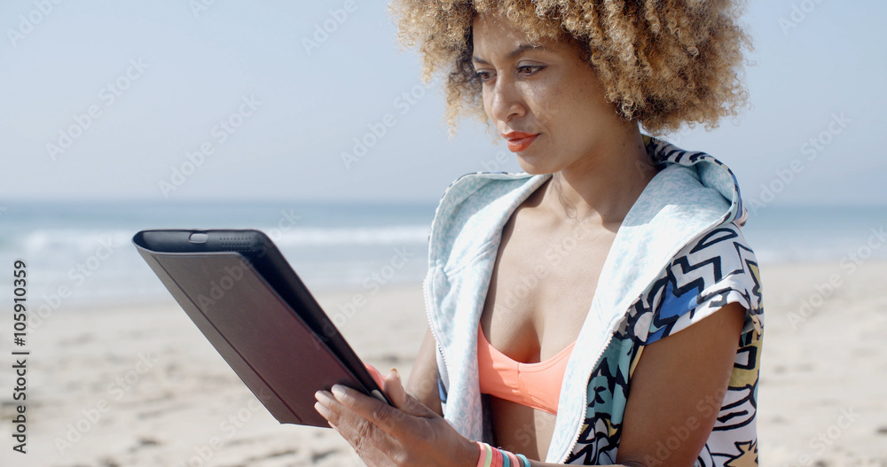 Pretty african-american girl using tablet pc at the beach on a sunny day Pretty african-american girl using tablet pc at the beach on a sunny day