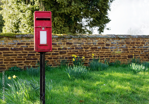 Red post box with green grass and stone wall in background