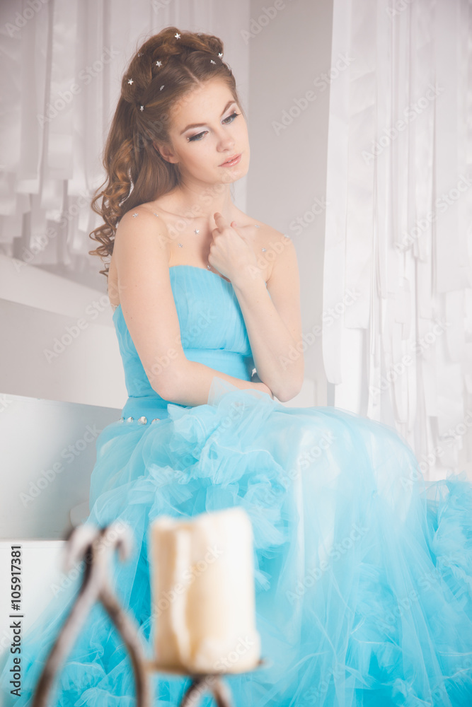 Beautiful young woman in gorgeous blue long dress like Cinderella with perfect make-up and hair style