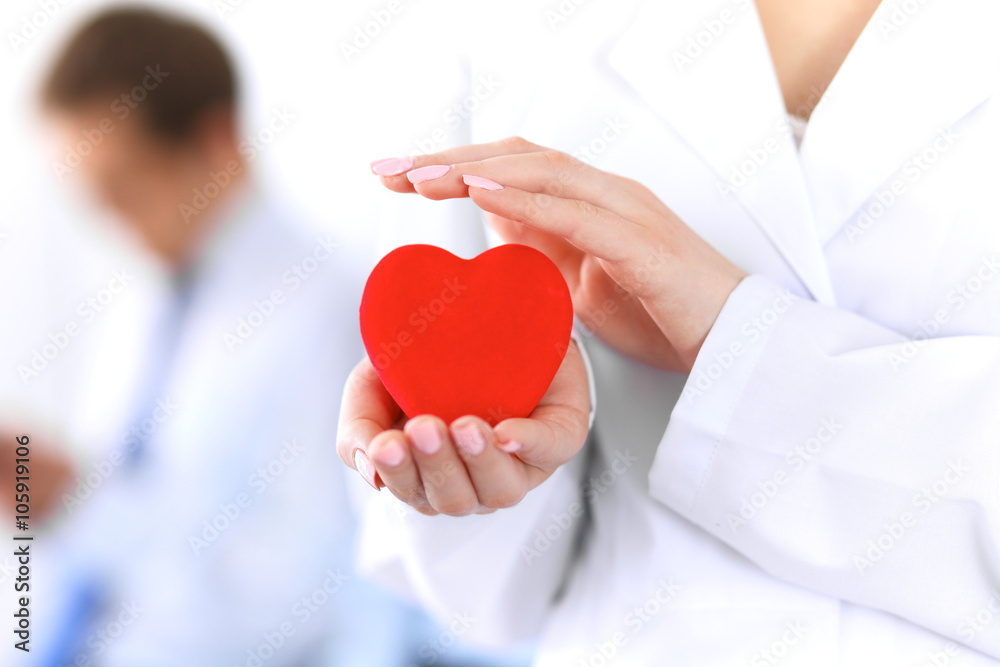 Femail doctor holding a red heart in his hands on a background of the patient. Health care concept Femail doctor holding a red heart in his hands on a background of the patient. Health care concept