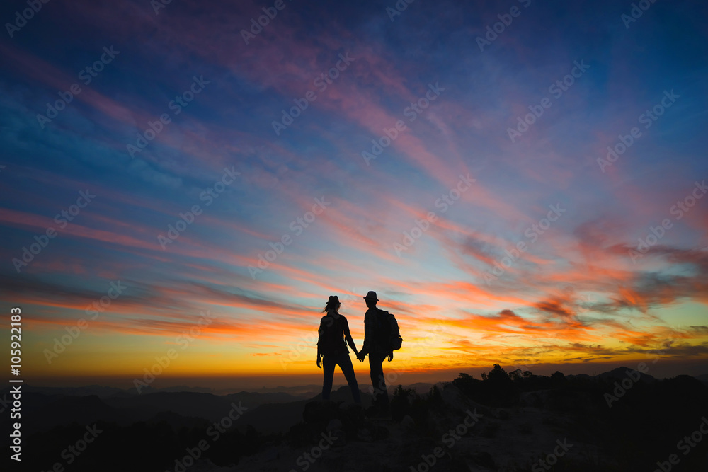 Silhouettes of two hikers with backpacks enjoying sunset view from top of a mountain. Travel concept
