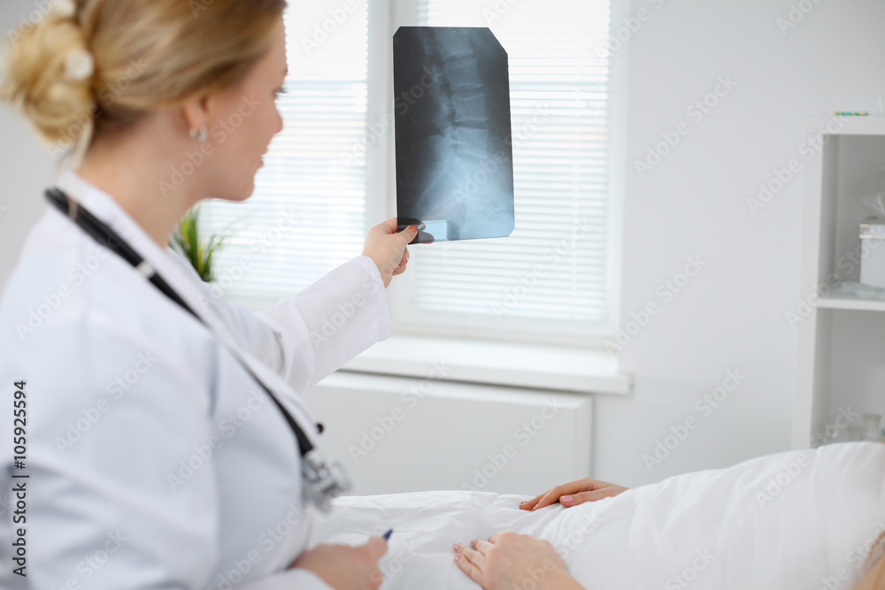 Female Doctor examines an X-ray picture of the spine next to patient lying in the bed in hospital Female Doctor examines an X-ray picture of the spine next to patient lying in the bed in hospital