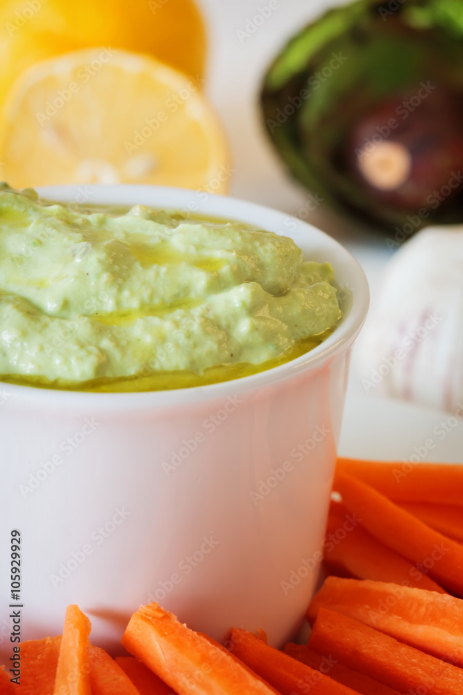 Fresh guacamole with carrot slices on a white wooden table Fresh guacamole with carrot slices on a white wooden table