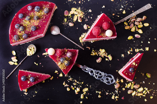 Pieces of delicious raspberry cake with fresh strawberries, raspberries, blueberry, currants and pistachios on black background. Free space for your text.