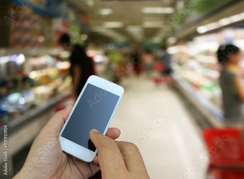 hand holding the smartphone on supermarket in blurry for backgro