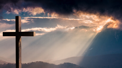 Jesus Christ cross. Easter, resurrection concept. Christian cross on a background with dramatic lighting, colorful mountain sunset, dark clouds and sky and sunbeams 