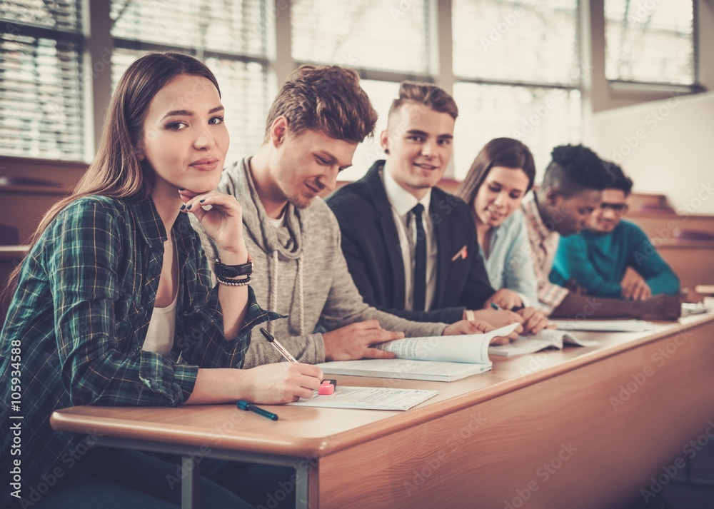 Multinational group of cheerful students taking an active part in a lesson while sitting in a lecture hall.