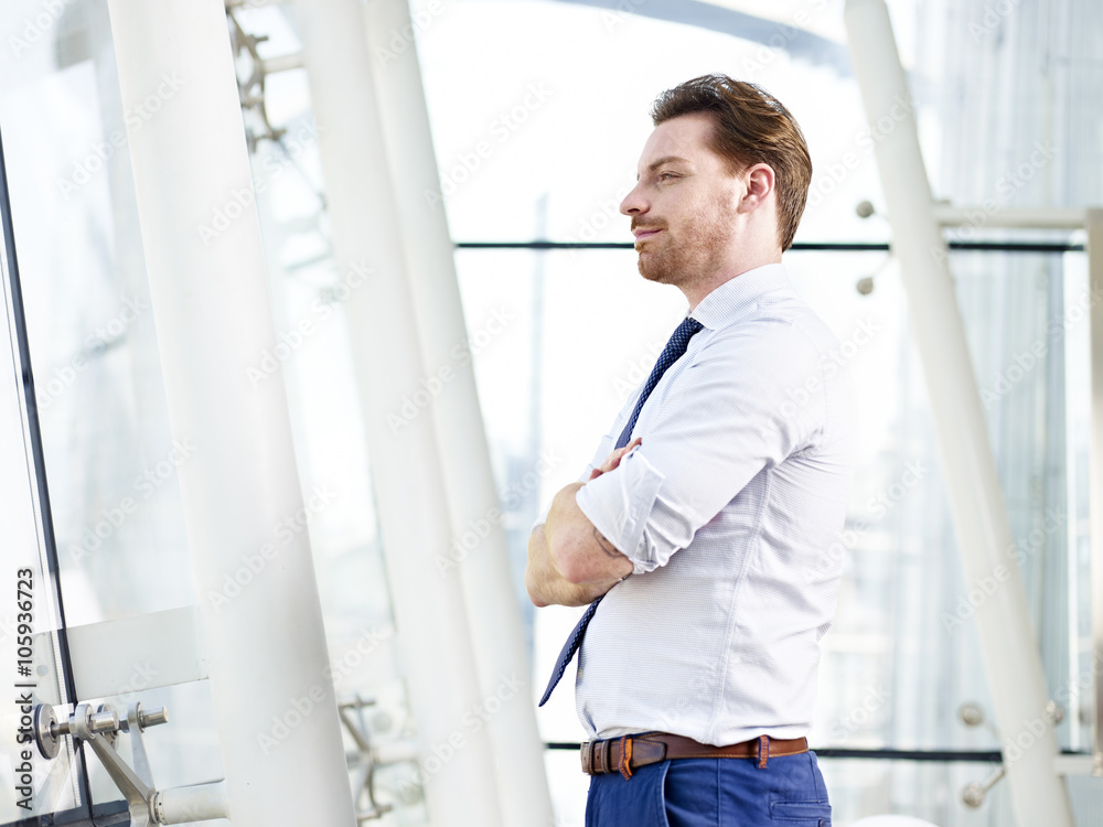 businessman standing by the window thinking businessman standing by the window thinking