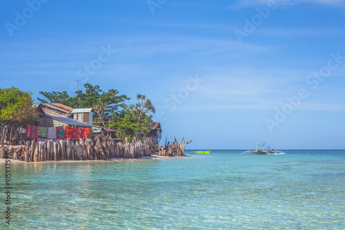 Tropical view of small traditional bamboo hut  hanging laundry  azure transparent water and clear blue sky. Mantigue Island  Philippines. Vacation and summer concept.  