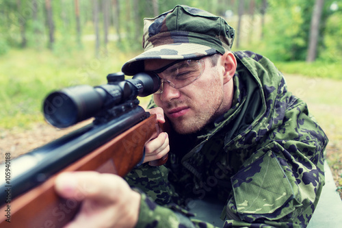 close up of soldier or hunter with gun in forest