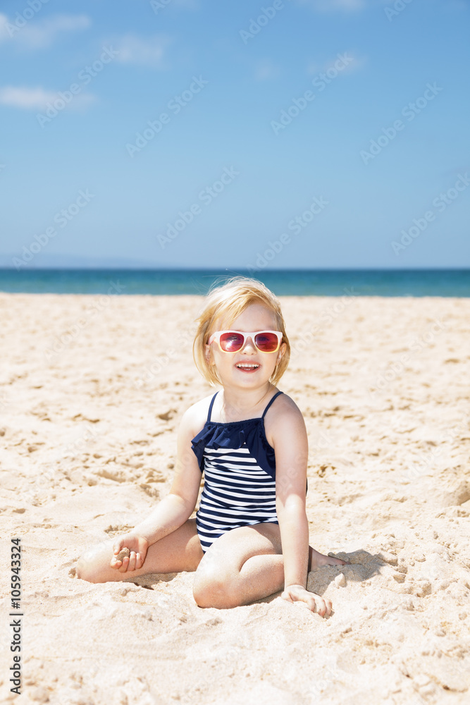 Happy girl in striped swimsuit playing with sand on white beach Happy girl in striped swimsuit playing with sand on white beach