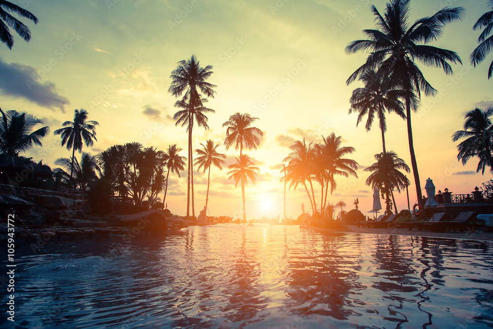 Obraz premium Złoty zmierzch na dennym wybrzeżu z drzewkami palmowymi odbicie w wodzie.