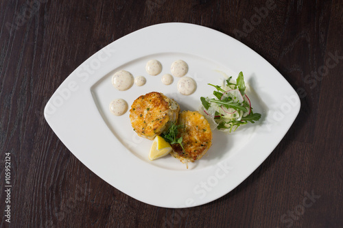 Beautiful fresh golden fish cakes, served with a wedge of lime, dill sauce and rocket on a white plate