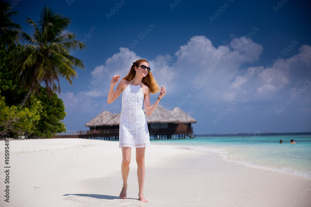 Young beautiful woman wearing sundress walking along the picturesque beach. Blue sky, coconut palms, white sand and azure water. Young beautiful woman wearing sundress walking along the picturesque beach. Blue sky, coconut palms, white sand and azure water.