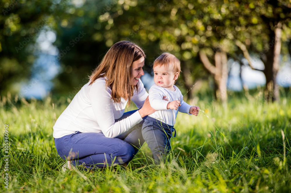 Fototapeta premium Mother holding her son making first steps, green nature