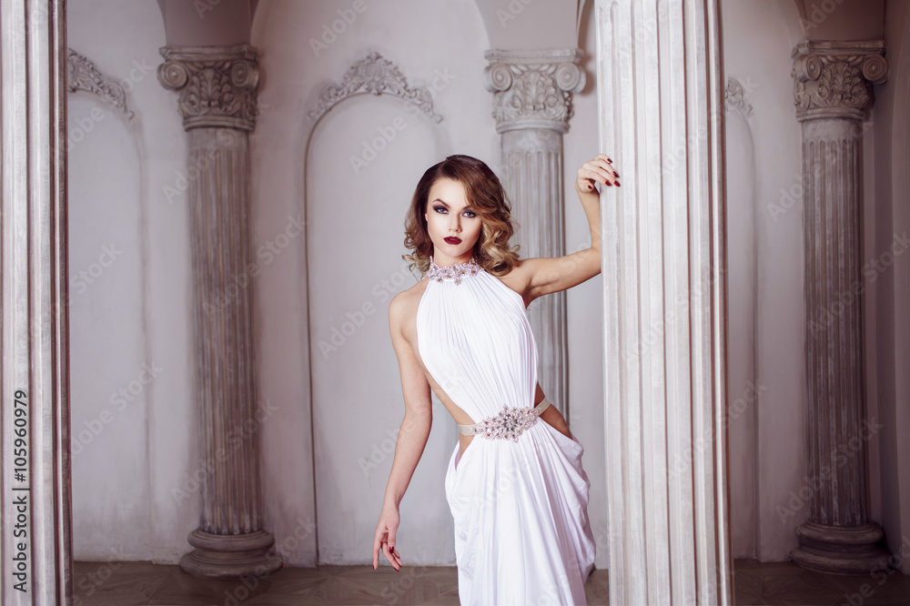 Fototapeta premium Portrait of young sexy woman in a white dress, luxurious hall with columns