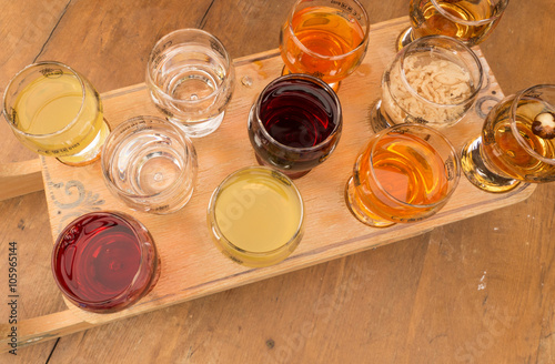 A group of glasses of various alcohol stacked on wooden board