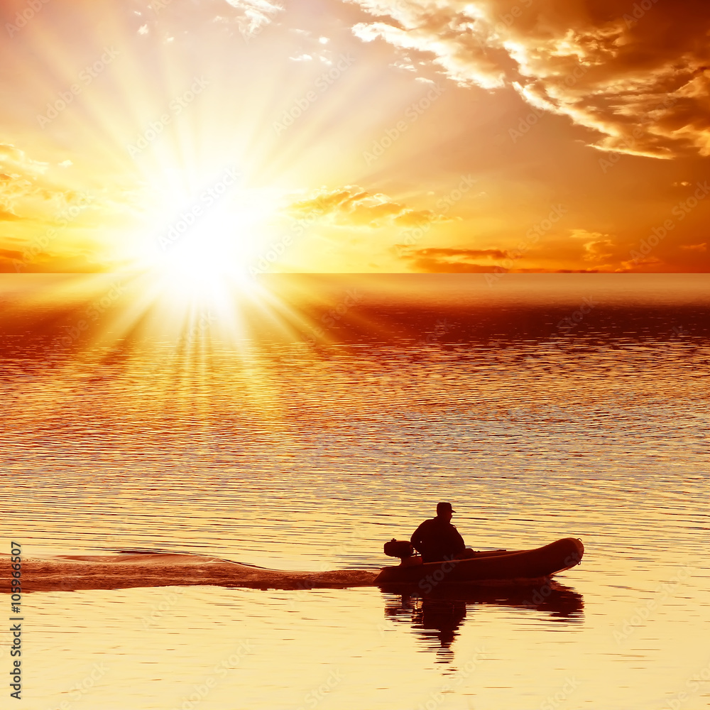 Man on a motor boat floats on the sea. On a background of a red sunset