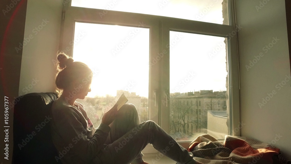 beautiful young woman sitting on window sill with coffee end reading book on background of sunset beautiful young woman sitting on window sill with coffee end reading book on background of sunset