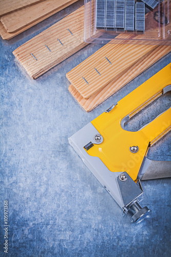 Yellow stapler gun metal staples wood planks on metallic backgro