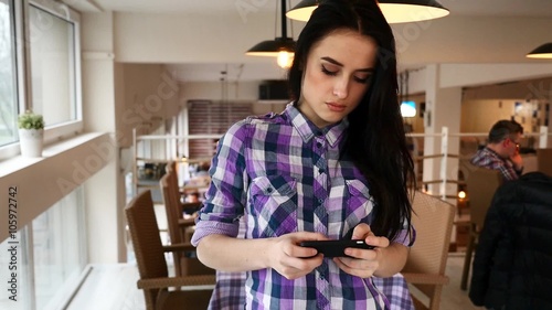 Young girl standing in the restaurand and using her mobile phone.  photo