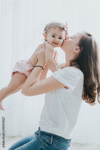 Beautiful mother portrait playing with her cute little girl in a white room in the morning