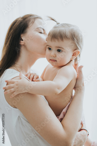 Beautiful mother portrait playing with her cute little girl in a white room in the morning